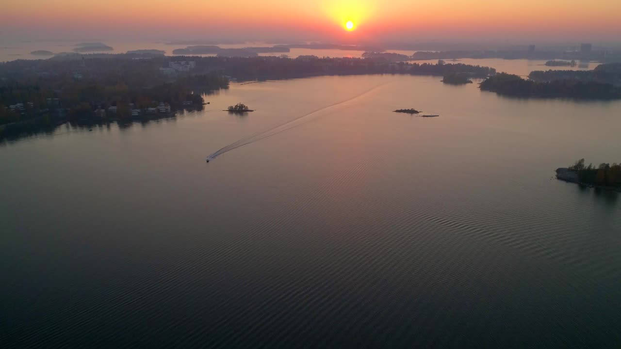 Aerial, drone shot, backwards over the sea, of a boat driving between hietalahti and keilaniemi, on seurasaarenselka, on a sunny and misty, autumn evening