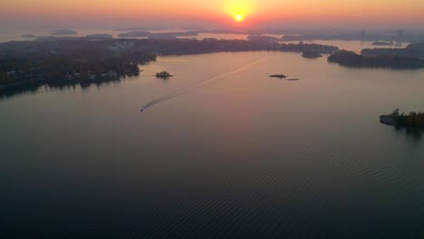 aerial, drone shot, backwards over the sea, of a boat driving between hietalahti and keilaniemi, on seurasaarenselka, on a sunny and misty, autumn evening