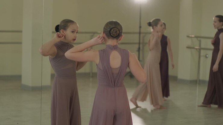 Un gruppo di giovani allievi di danza classica in abbigliamento da ballo nero che eseguono esercizi in un ampio studio di danza con pavimenti in legno e barre a muro. Espressioni concentrate e movimenti sincronizzati