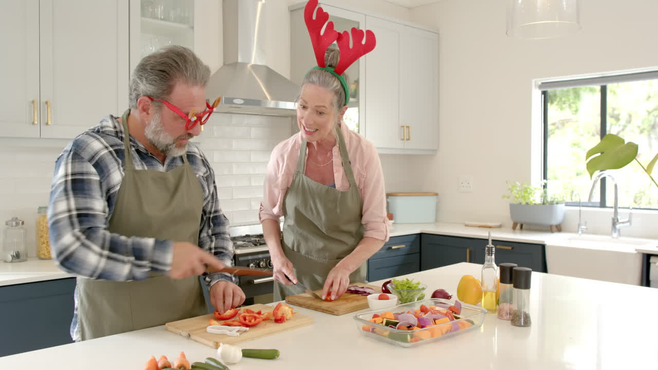 At Christmas, Mature couple wearing festive accessories preparing vegetables together in kitchen