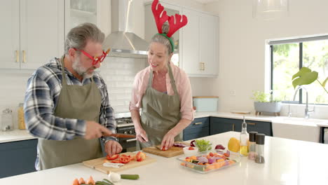 at christmas, mature couple wearing festive accessories preparing vegetables together in kitchen