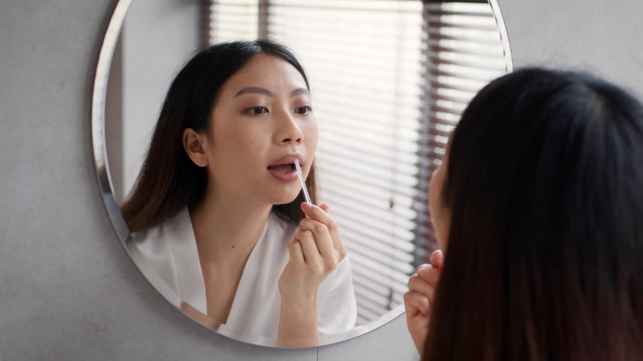 Woman Applying Lipstick in Front of Mirror