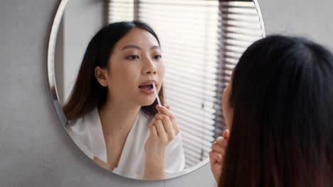 mujer aplicando lápiz labial frente al espejo