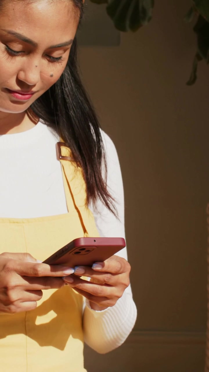 Vertical video: Scrolling woman lowering red phone onto lap at home, resting hands in yellow dress