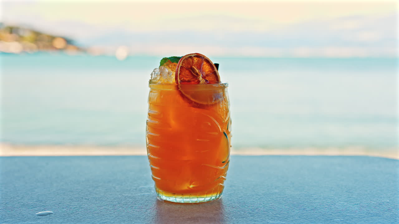Close up of an orange cocktail on a table with a blurred view of the sea on the background