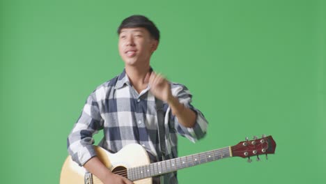 young asian teen boy with guitar and rapping on the green screen background