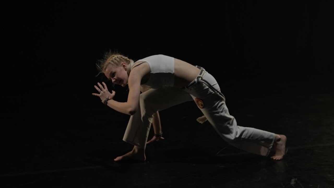 Group of a professional dancers are practicing capoeira in darkness against a spotlight on a black background of studio. Afro-Brazilian martial art that combine elements of dance.