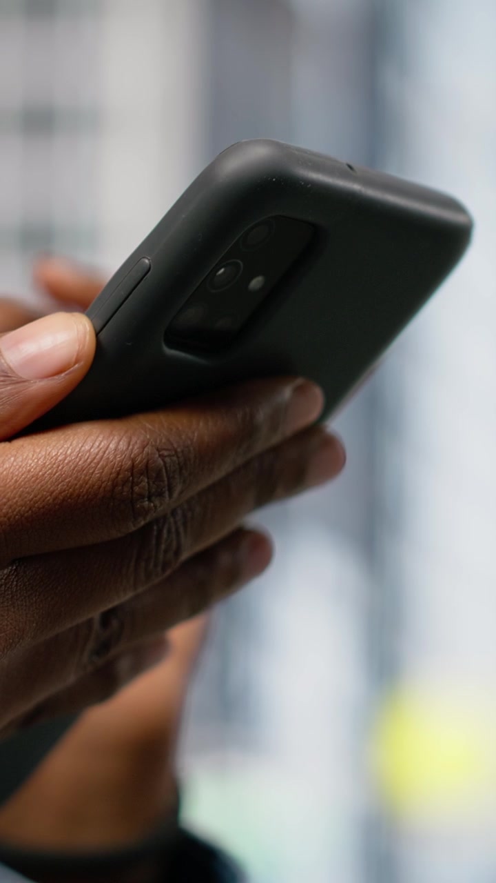 Video verticale. Primo piano di una donna che naviga sul web con il cellulare mentre cammina per una strada cittadina.