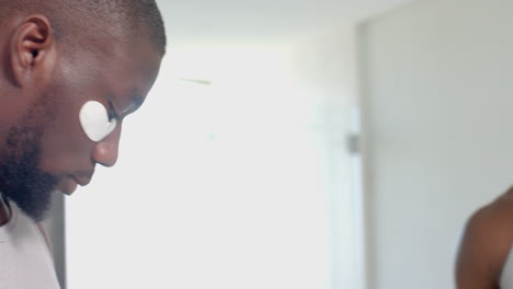 applying under-eye patches, african american man enjoying skincare routine at home spa