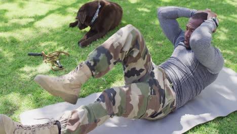 african american male soldier exercising and doing sit ups with dog in garden