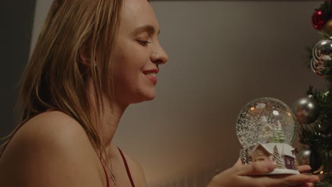 una mujer bonita sacude un globo de nieve con tema de navidad y sonríe mientras cae la nieve