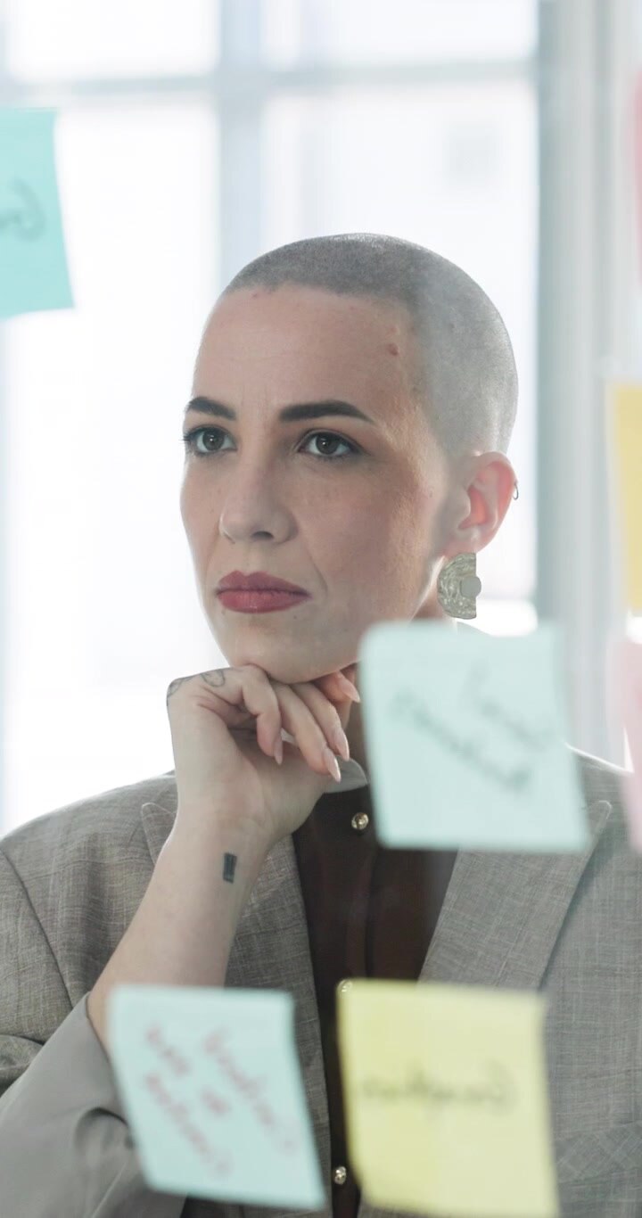 Donna professionista che fa brainstorming con post-it su parete di vetro