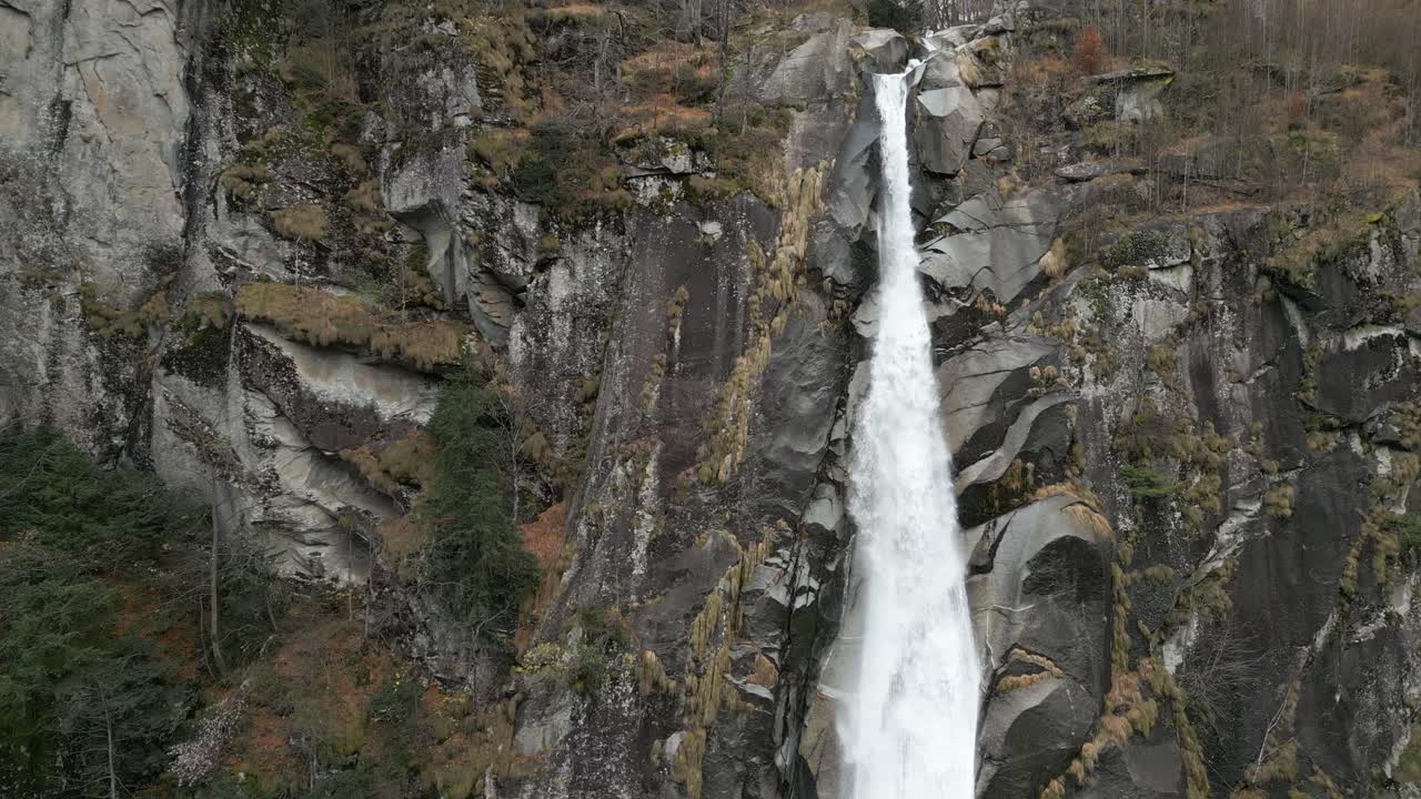 un disparo frontal de una cascada que comienza en su fuente y cae por las rocas negras