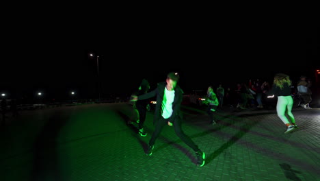contemporary hip hop dancers at the night square. race cars at backdrop with the headlights on.