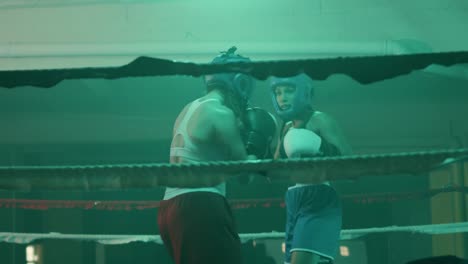 two female boxers in helmets and boxing gloves fighting in ring at gym