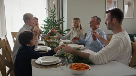 Kaukasische-Mehrgenerationenfamilie-Sitzt-Um-Den-Tisch,-Hält-Händchen-Und-Betet.