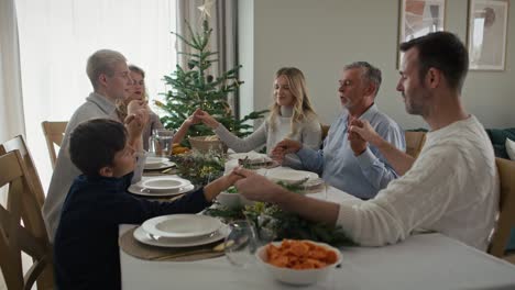 caucasian multi generation family sitting around the table, holding hands and praying.