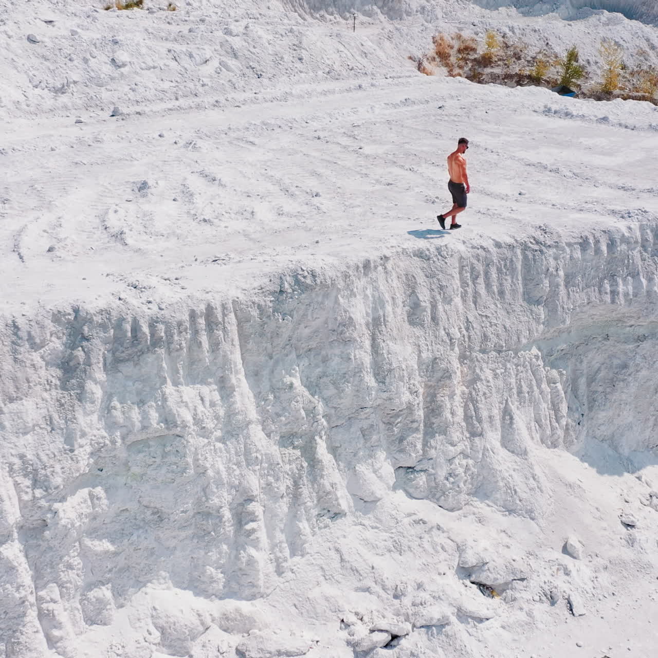 Bodybuilder in the mountains. Athletic man walking along the white rocky canyon. Sportsman in shorts doing exercises on white hill in summer. Aerial view.