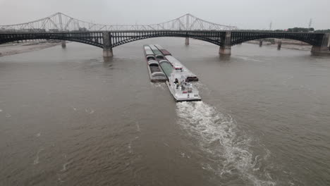 Low-aerial-parallax-of-tugboat-pushing-barges-up-Mississippi-River-under-bridge