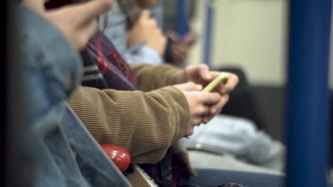 close up of people sitting on subway using smartphone