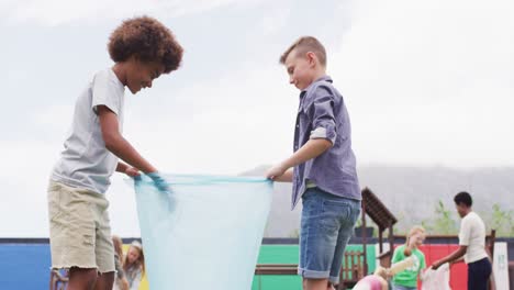 Vielfältige-Lehrerin-Und-Glückliche-Schulkinder,-Die-Gemeinsam-Mit-Taschen-Auf-Dem-Schulhof-Putzen