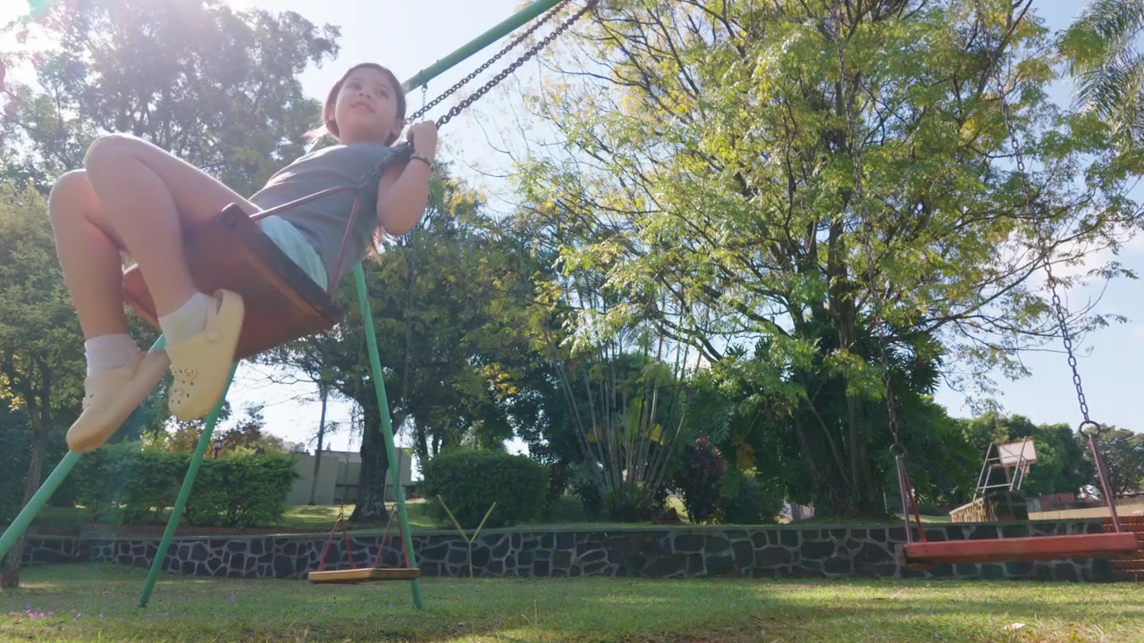 Una niña se columpia alegremente bajo árboles bañados por el sol en un entorno de parque. Ideal para contenido familiar o promociones de estilo de vida al aire libre.