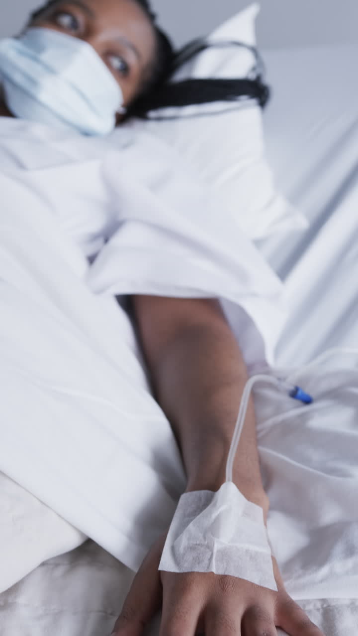 Vertical video of african american female patient in bed in hospital room, slow motion