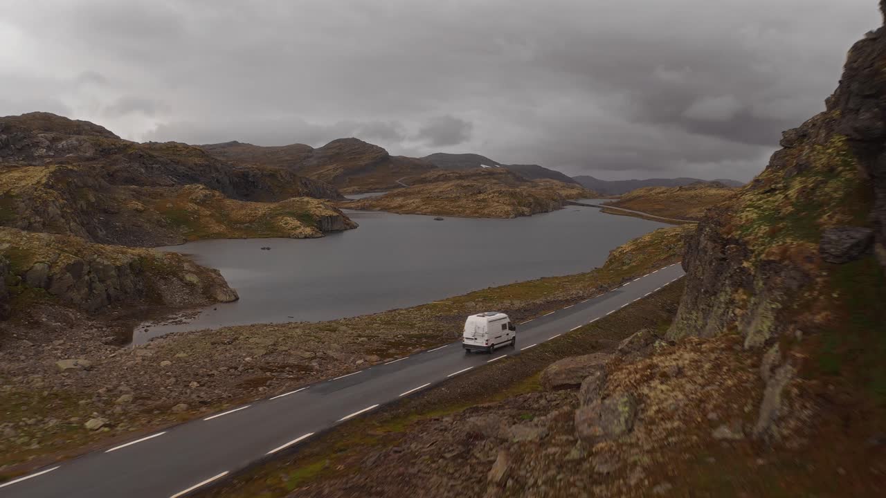 A camper van driving on a road along a scenic mountain and lake landscape in Norway