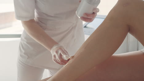 aesthetician is processing procedure of hair removal in clinic cosmetologist is smearing leg skin