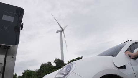 progressive woman recharge ev from charging station generated by wind turbine.