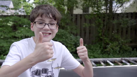 cute boy sitting on trampoline smiles and gives camera thumbs up