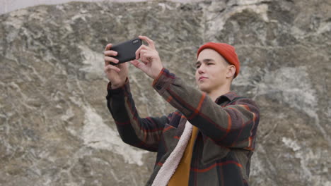 teenage boy with orange beanie and winter clothes looking at smartphone on the mountain