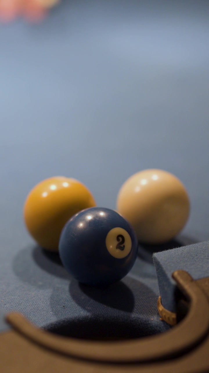 Multiple pool balls roll toward a corner pocket on blue felt under soft, low lighting
