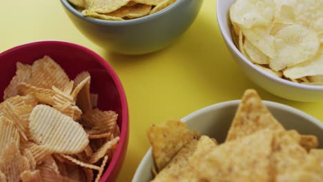 close up of four bowls full of variety of chips on yellow surface