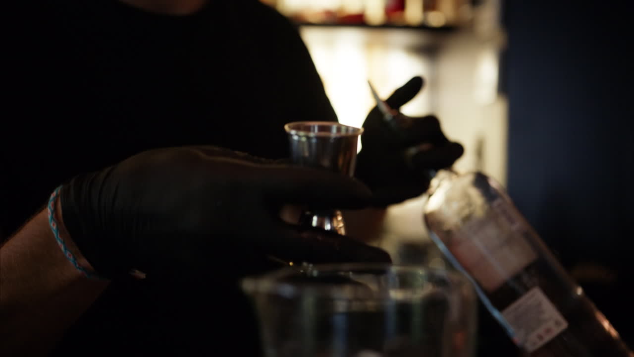 Barman che versa alcol in un bicchiere con cubetti di ghiaccio