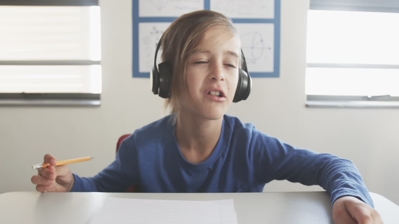 A scuola, un ragazzo con le cuffie scrive su un blocco note in classe.