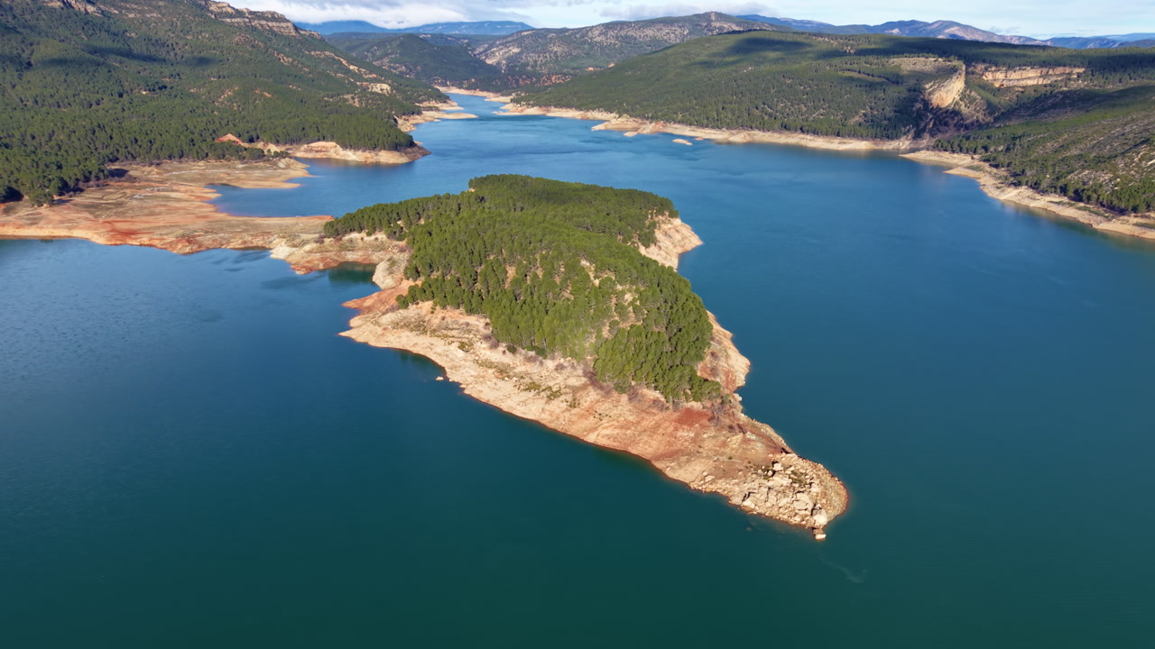 Forested peninsula jutting into a turquoise reservoir surrounded by pine-covered hills and rocky cliffs in Spain