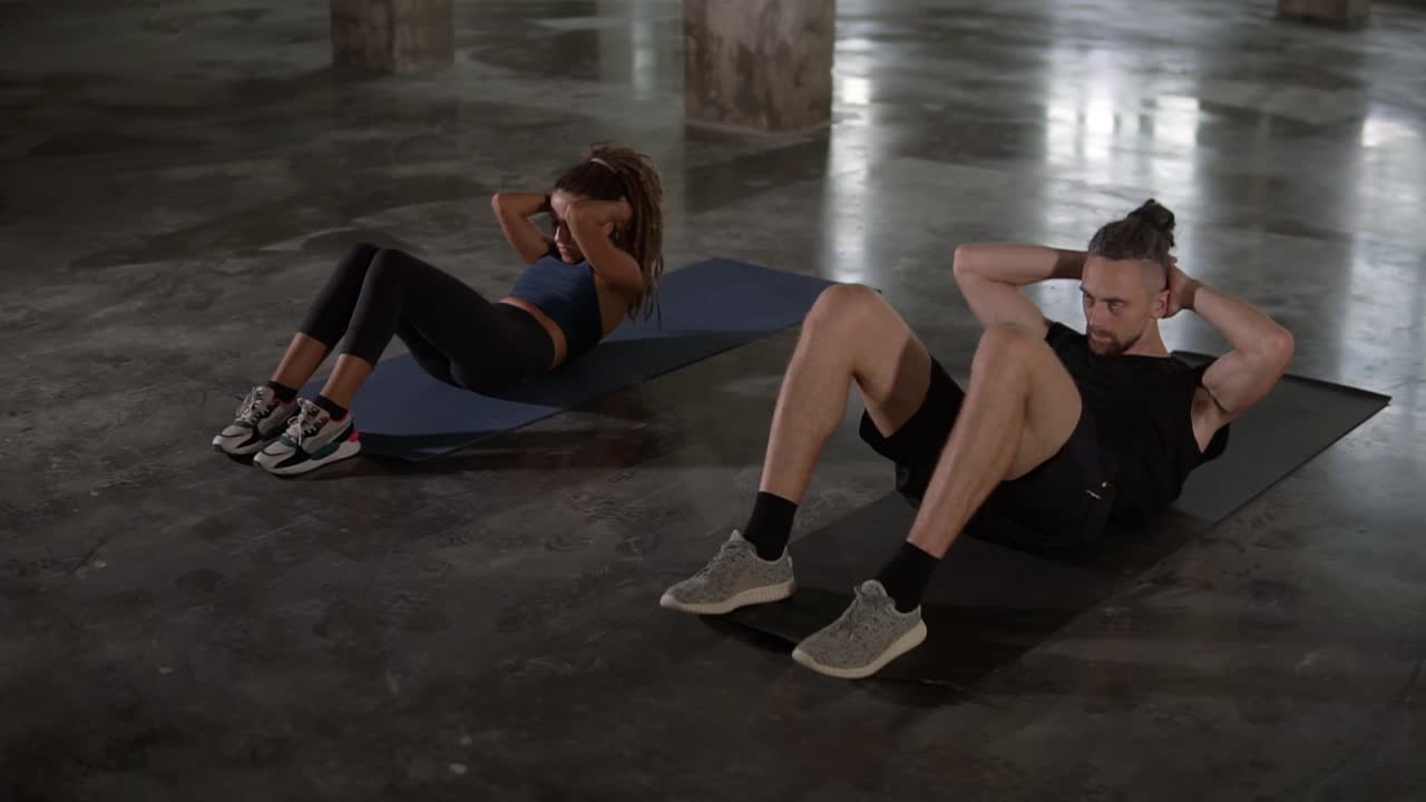 joven hombre y mujer elegantes en ropa deportiva entrenando en un estudio vacío, haciendo abdominales sincrónicos juntos, fuertes y saludables, mantener un estilo de vida activo, trabajar duro para ponerse en forma, cámara lenta