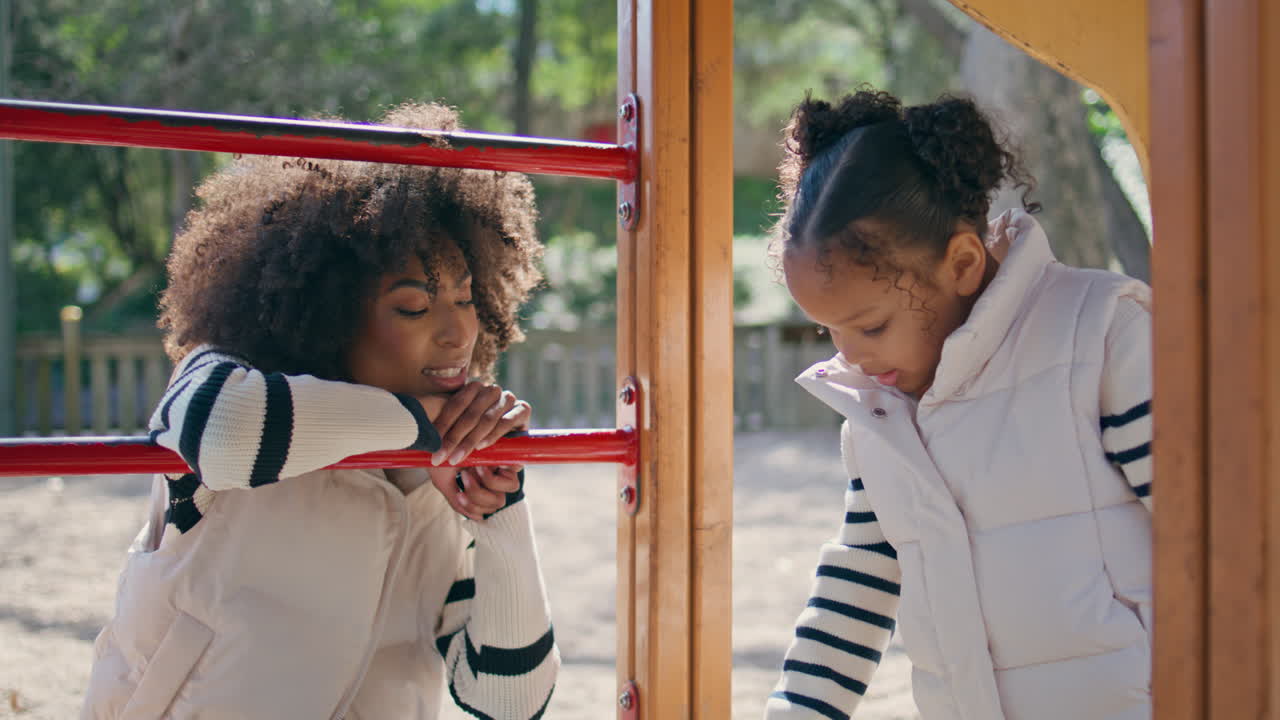 madre viendo a su hija jugando en el patio de recreo de cerca. fin de semana familiar despreocupado
