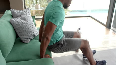strong and fit man doing tricep dips on green couch in modern living room