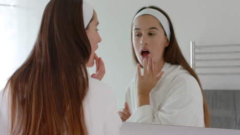 applying skincare product, woman in bathrobe looking in mirror at home spa