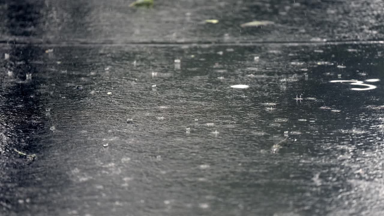 Intense rain pelting asphalt in slow motion, creating ripples and splashes