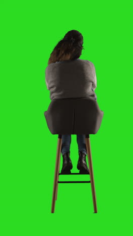 woman sitting on a chair in front of a green screen