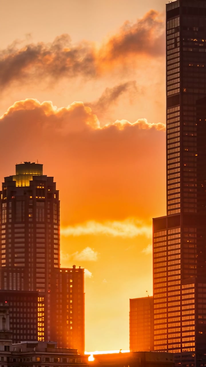 Vertical video: Drifting clouds dimming sun between towers at urban skyline, highlighting windows