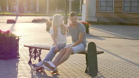couple sitting on a bench in the park with skateboards