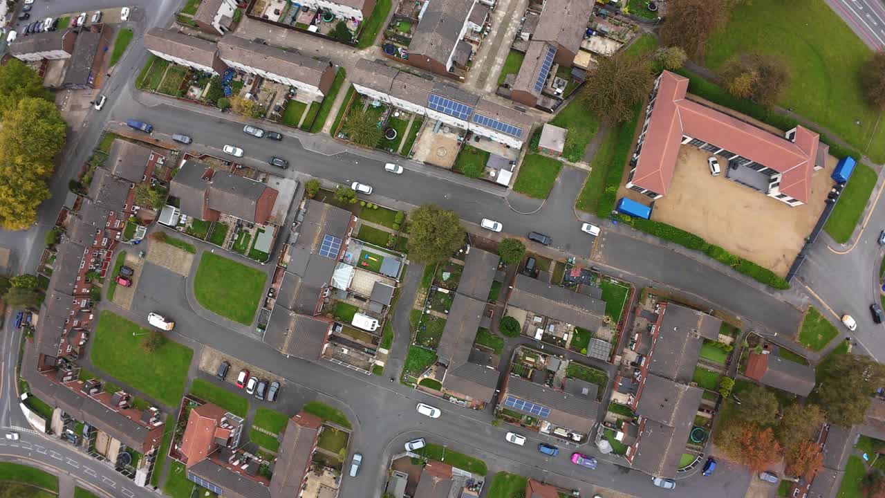 Luftfoto fra drone af boligtag i Leeds, der viser rækkehuse, skole med legeplads, parkerede biler langs smalle gader, små haver, grønne pletter, efterårstræer, oversigtskortlægningsperspektiv.