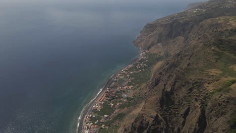 aerial view of the calheta parish in the madeira island, drone rotating showing the the showing the contrast between the village near the sea and the mountains in the background