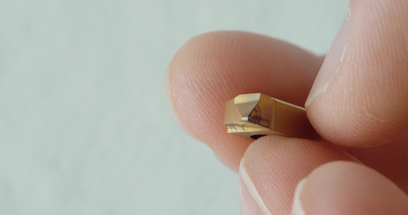 Primer plano macro de una mano sosteniendo un inserto de corte indexable desgastado, mostrando el desgaste de la herramienta, el daño por mecanizado, la inspección metalúrgica y el mantenimiento industrial.