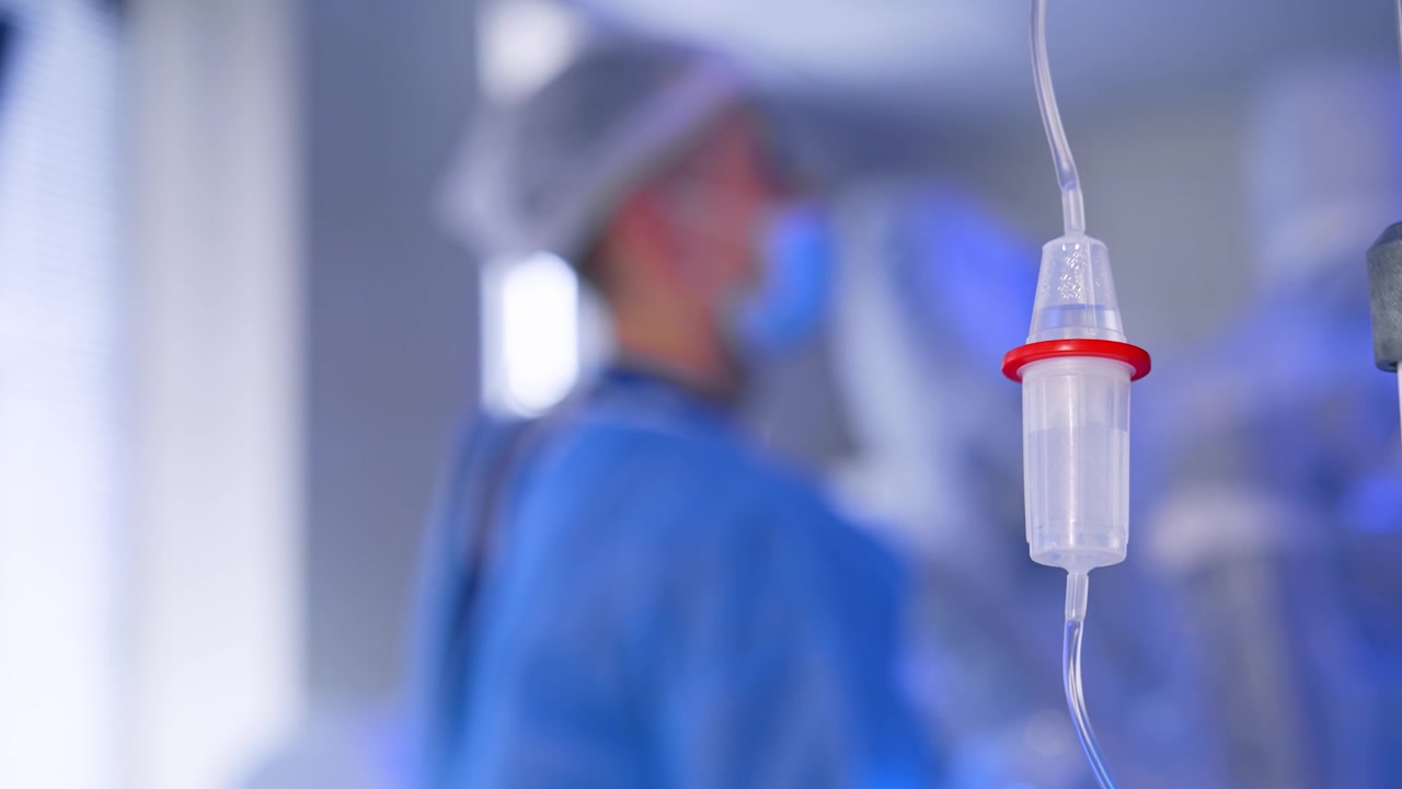 Flebo con soluzione fisiologica nella sala operatoria. Primo piano. Immagine sfocata di un medico in uniforme blu sullo sfondo.