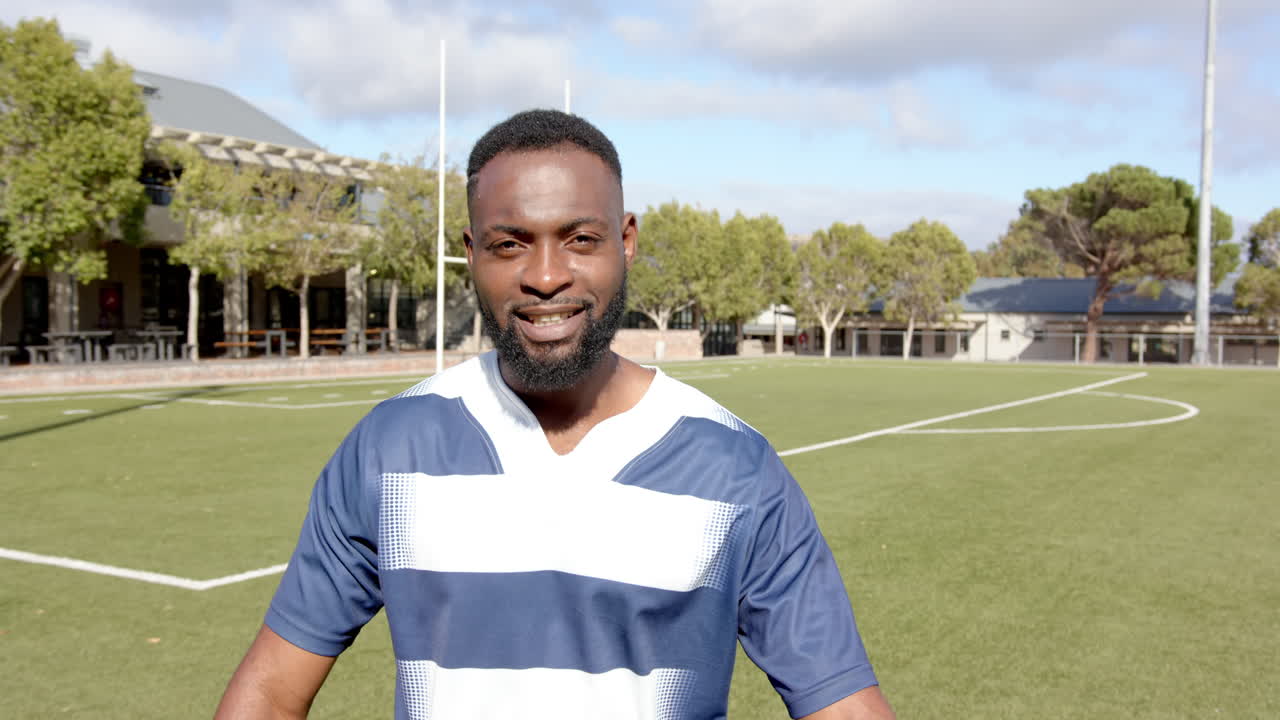 Atleta masculino afro-americano sorrindo, de uniforme esportivo em campo de futebol, fitness, com espaço para texto.